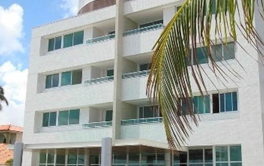 Foto da fachada de um prédio branco com sacadas e uma folha de coqueiro em destaque na lateral.