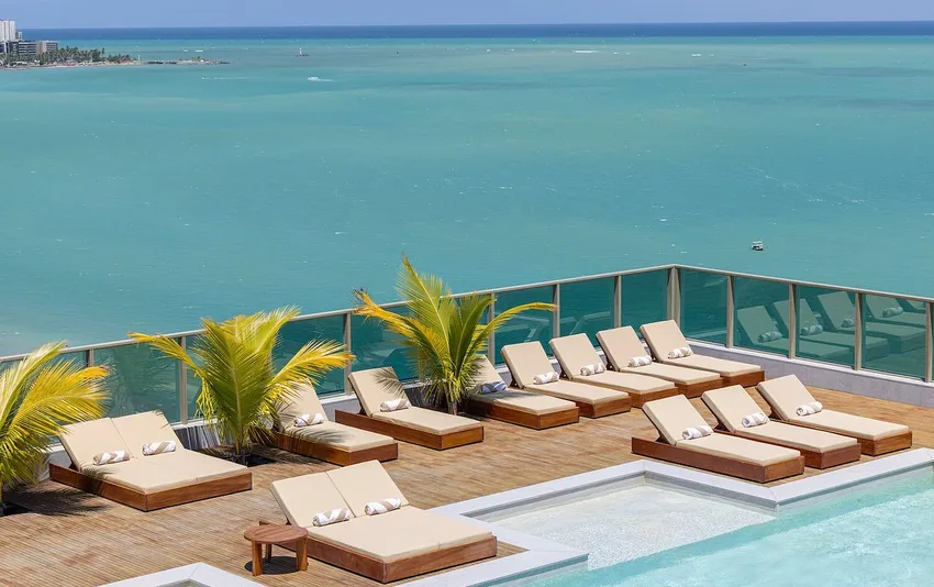 Foto de área de descanso com espreguiçadeiras ao lado da piscina e vista para o mar.