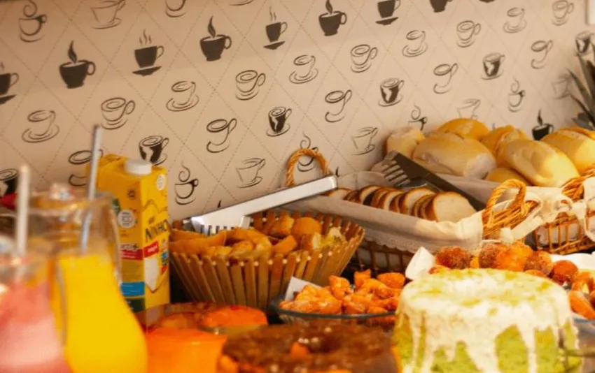 Foto de mesa com itens do café da manhã, incluindo pães, bolos, salgados e bebidas