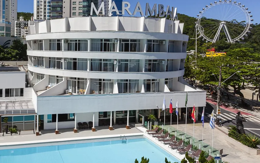 Foto da fachada de um hotel redondo com piscina em primeiro plano e uma roda-gigante ao fundo
