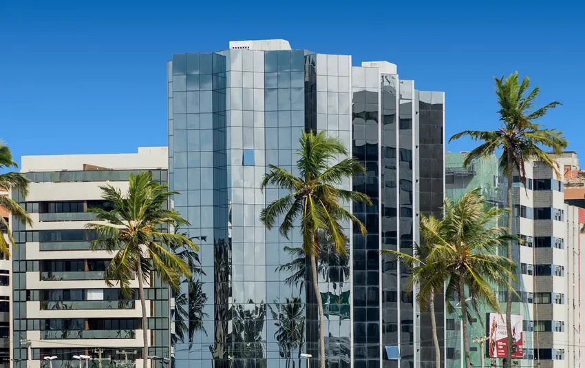Foto da fachada de prédio comercial com coqueiros.