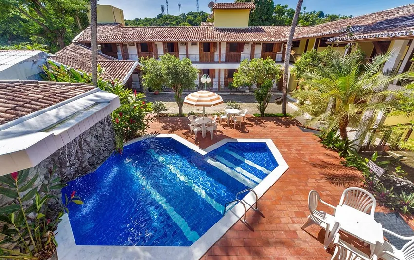 Foto da piscina da pousada com área de lazer, jardins e mesas ao redor