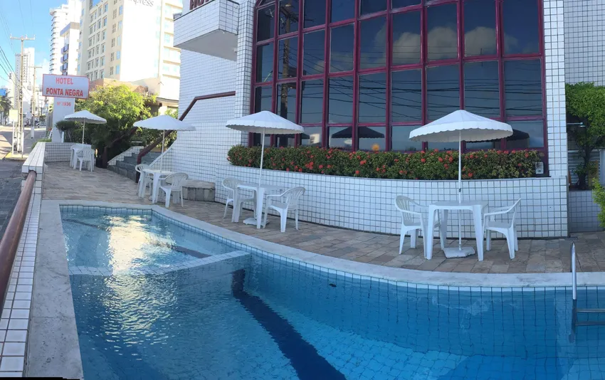 Foto da área da piscina do hotel, com mesas e guarda-sóis distribuídos ao redor