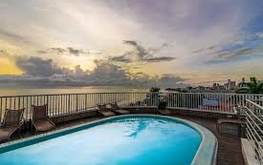 Foto de uma piscina no terraço com espreguiçadeiras ao redor e vista para o mar durante o pôr do sol