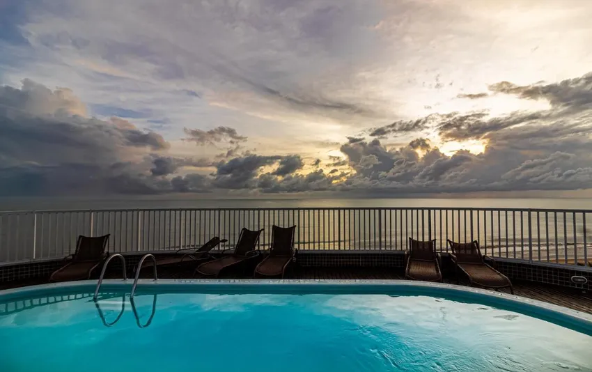 Foto de uma piscina no terraço com espreguiçadeiras e vista para o mar ao pôr do sol