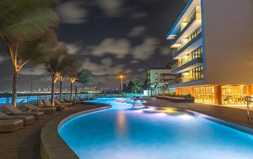 Foto de uma piscina de hotel iluminada à noite com espreguiçadeiras