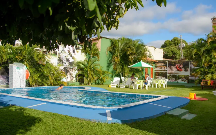 Foto da piscina do hotel com guarda-sol, cadeiras e área de descanso.