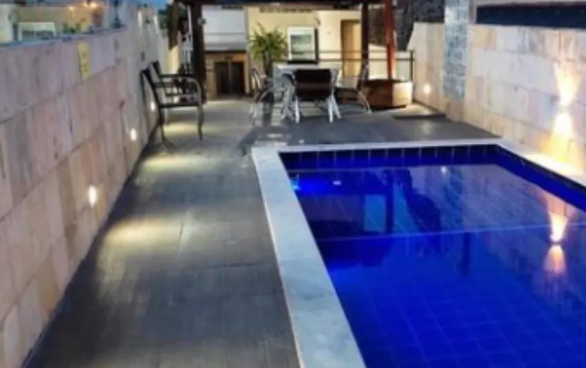 Foto de piscina iluminada durante a noite, com mesas e cadeiras ao fund
