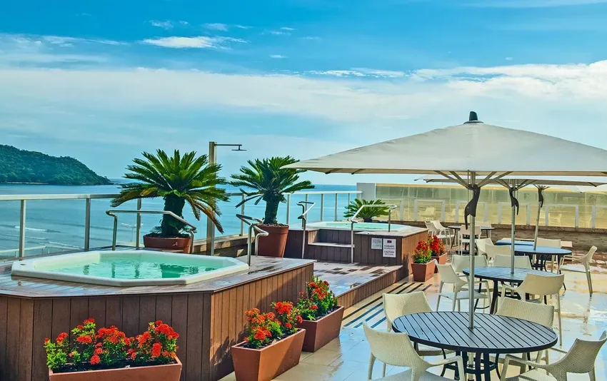 Foto de um terraço ensolarado com banheiras de hidromassagem, mesas com guarda-sóis e vista para o mar