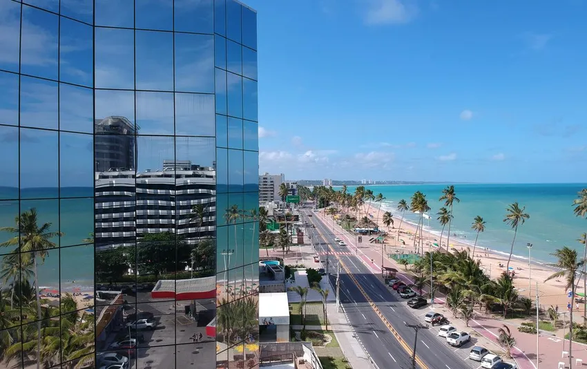 Foto da orla com avenida, praia e prédio espelhado